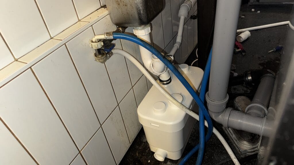 Plumber installing a commercial sink macerator in a restaurant kitchen to improve wastewater drainage in NW6, London.